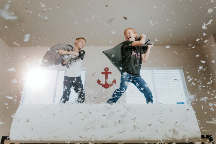 two kids having a pillow fight on a bed