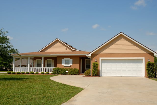 A clean concrete driveway in from of a light brown home